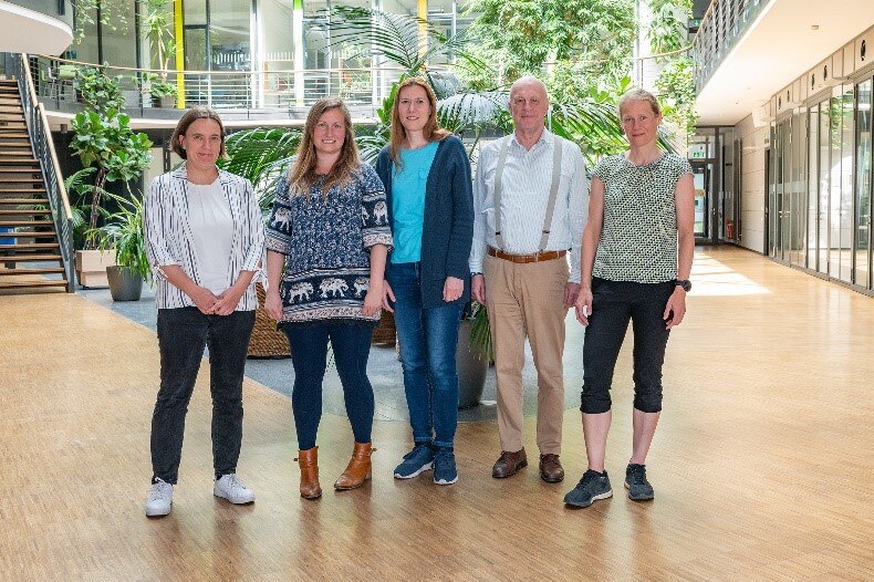 Vier Frauen und ein Mann stehen in einem lichten Raum vor einigen Pflanenkübeln.